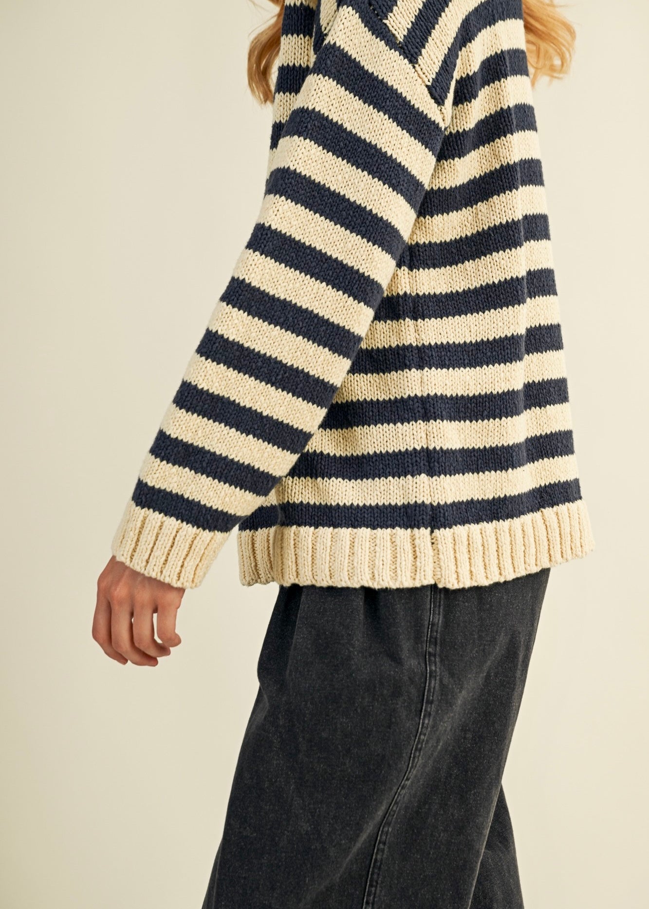 Person wearing a striped sweater with navy and beige colors on a plain background