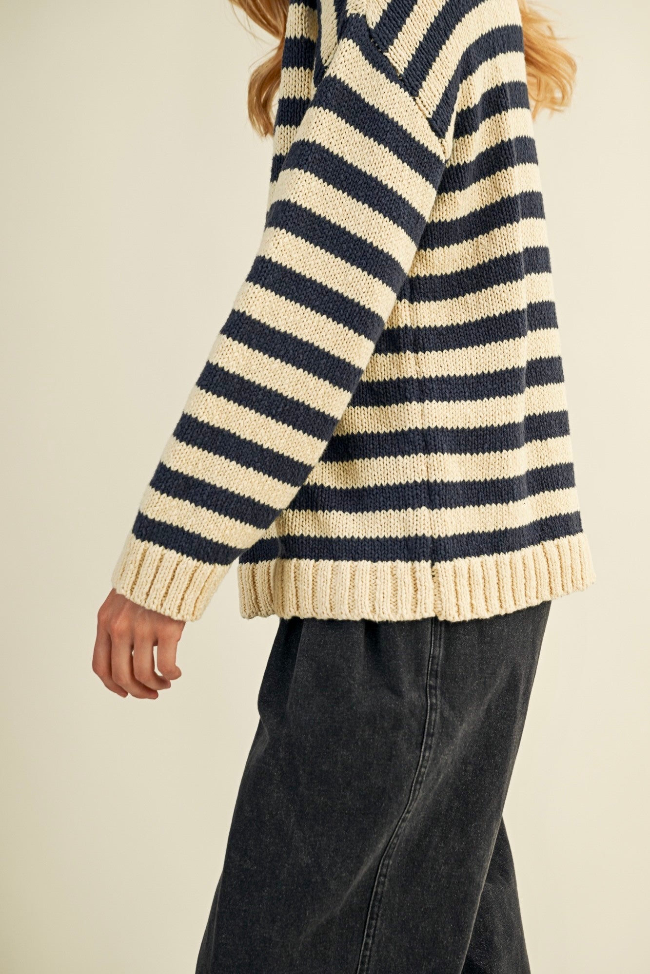 Person wearing a striped sweater with navy and beige colors on a plain background