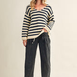 Woman wearing a striped sweater and dark pants on a beige background