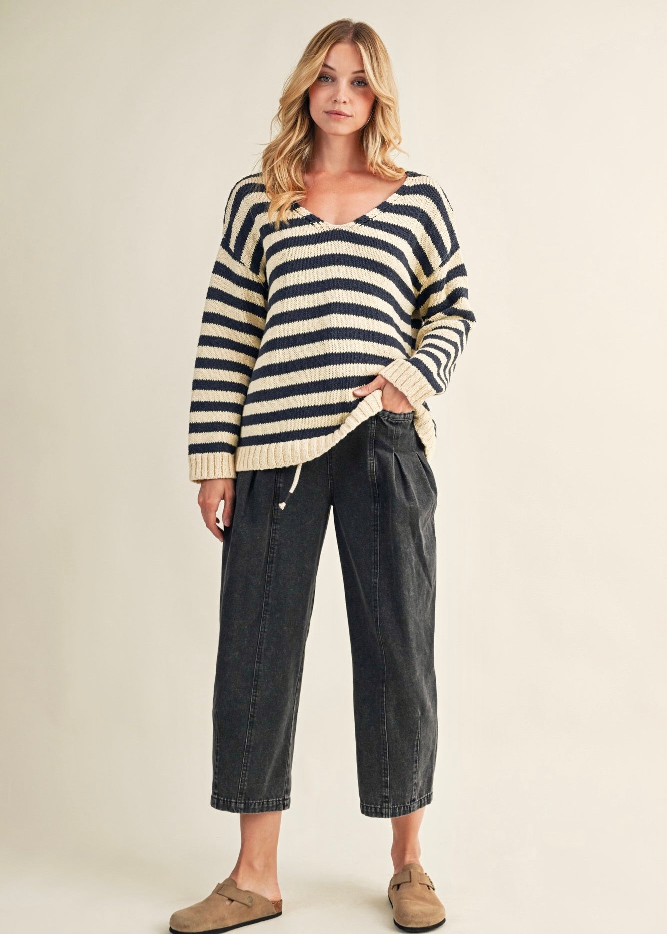 Woman wearing a striped sweater and dark pants on a beige background