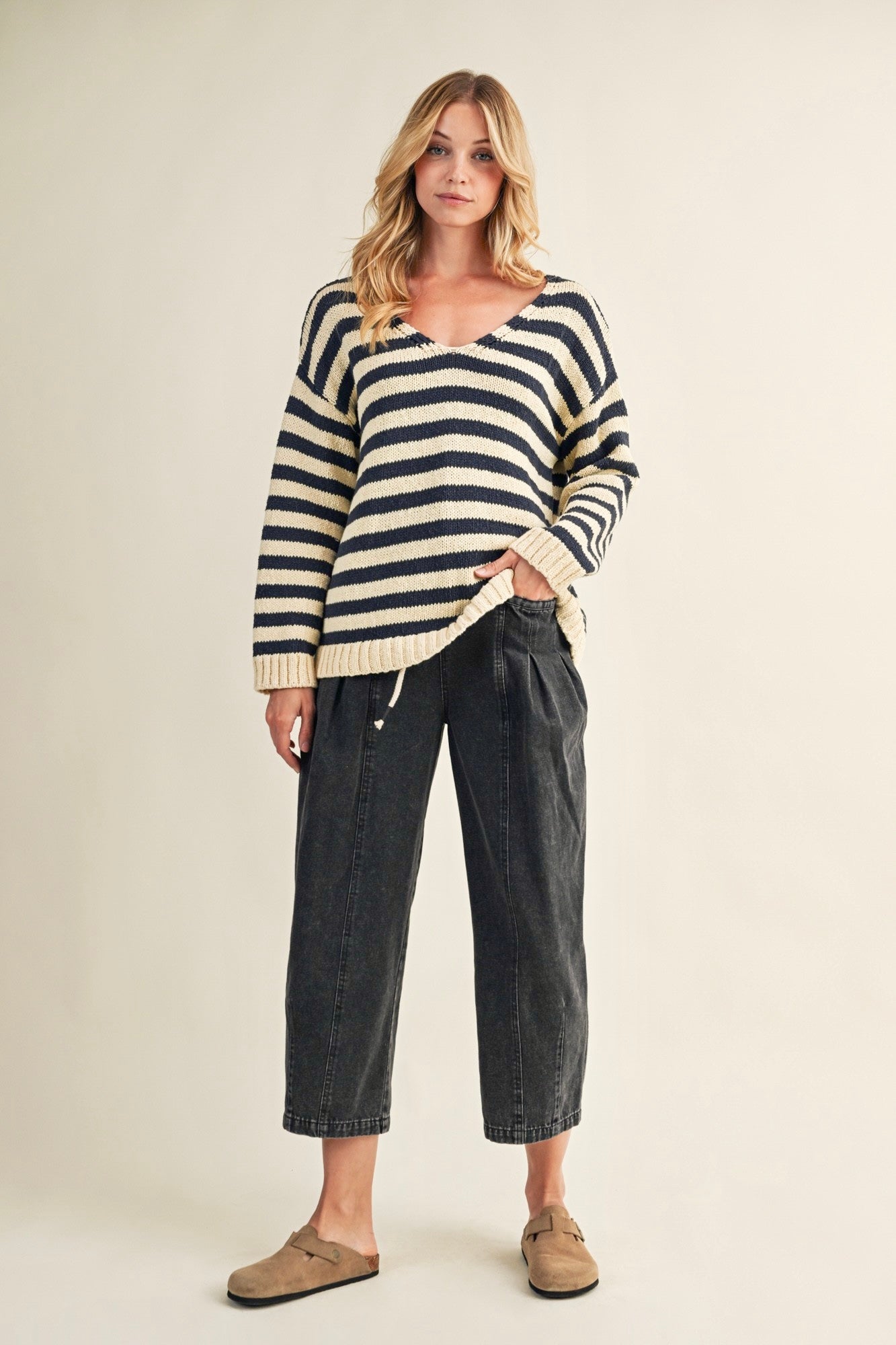 Woman wearing a striped sweater and dark pants on a beige background