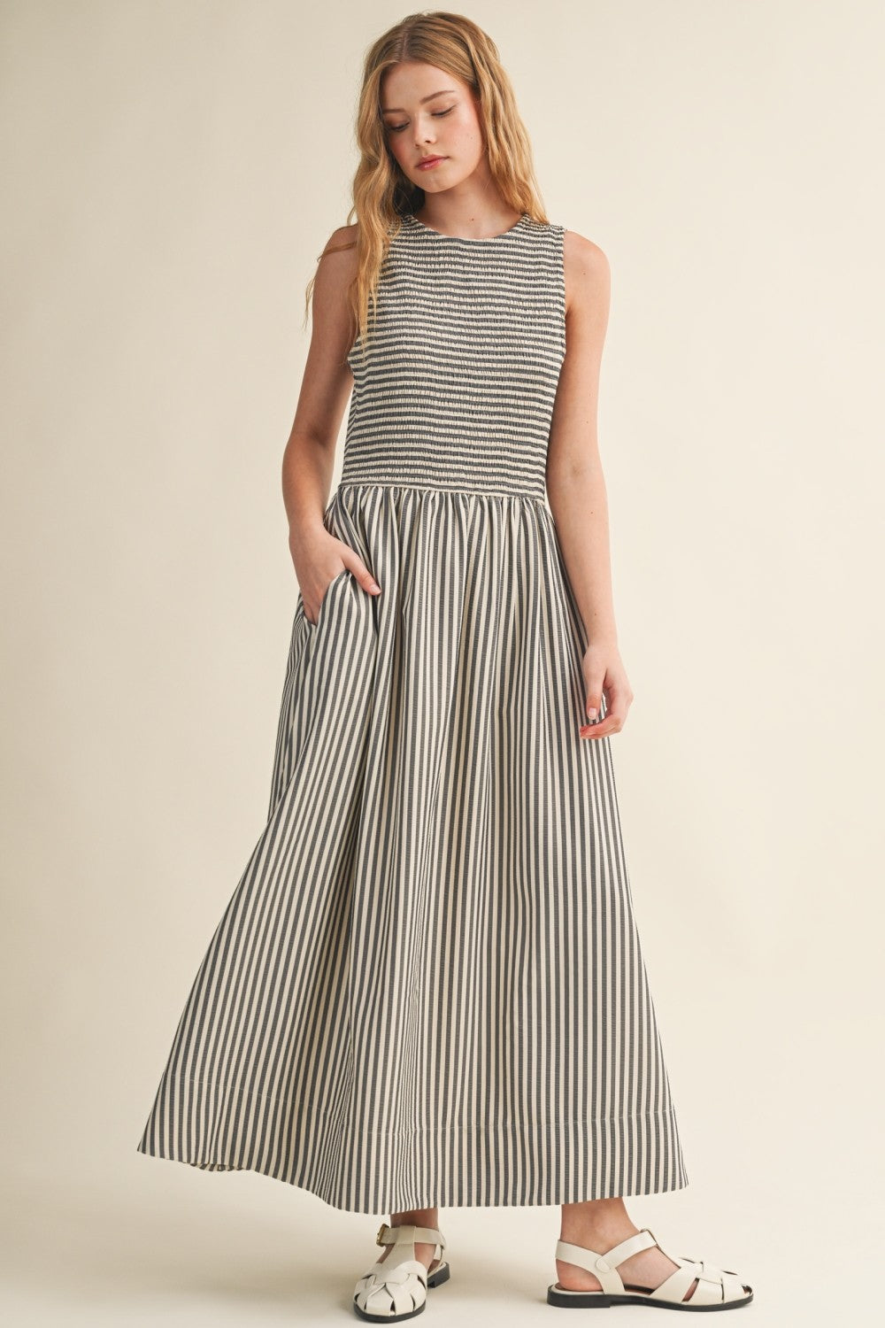 Darcy Smocked Stripe Maxi Dress in black and ivory stripe, full-length front view with sleeveless smocked bodice and model showing side pockets.