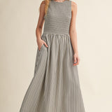 Darcy Smocked Stripe Maxi Dress in black and ivory stripe, full-length front view with sleeveless smocked bodice and model showing side pockets.