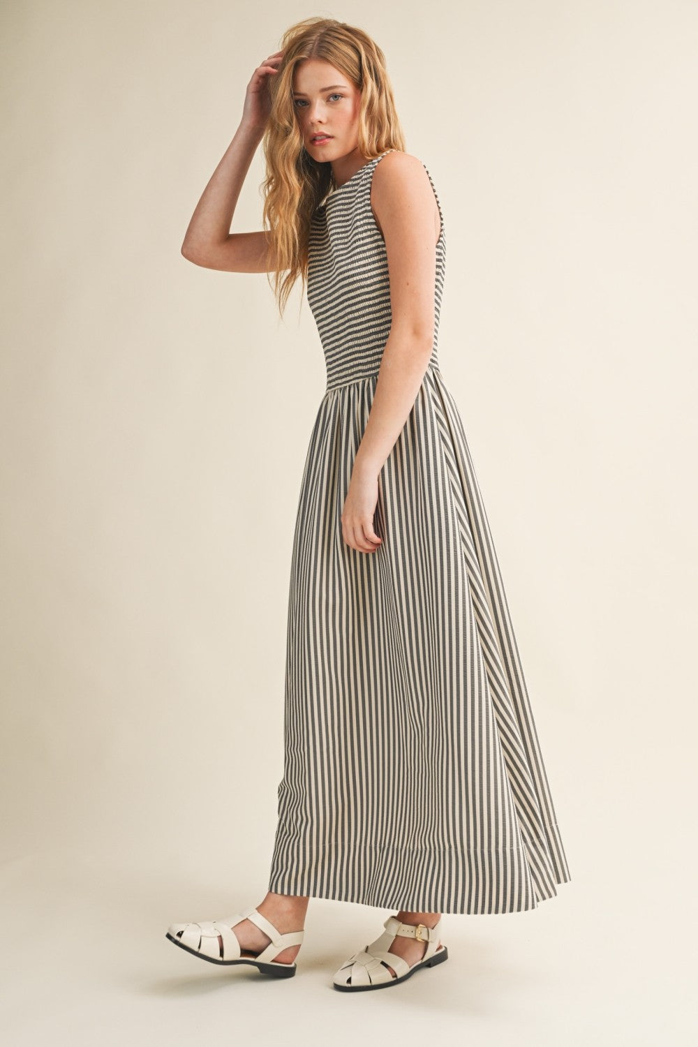 Side view of Darcy Smocked Stripe Maxi Dress in black and ivory stripe with sleeveless smocked bodice, flowing maxi skirt, and side pockets.