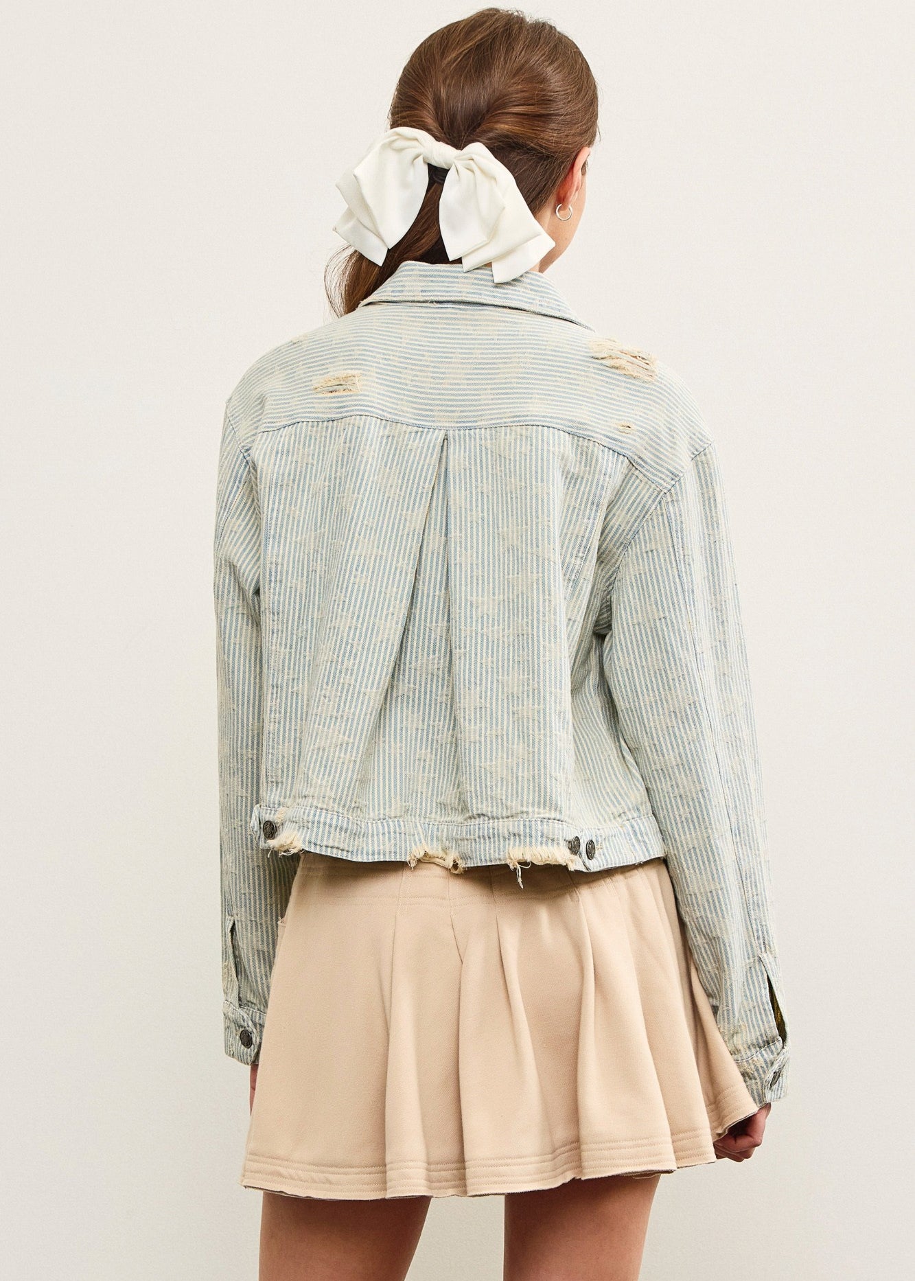Back view of distressed hem striped denim jacket with pleated back detail