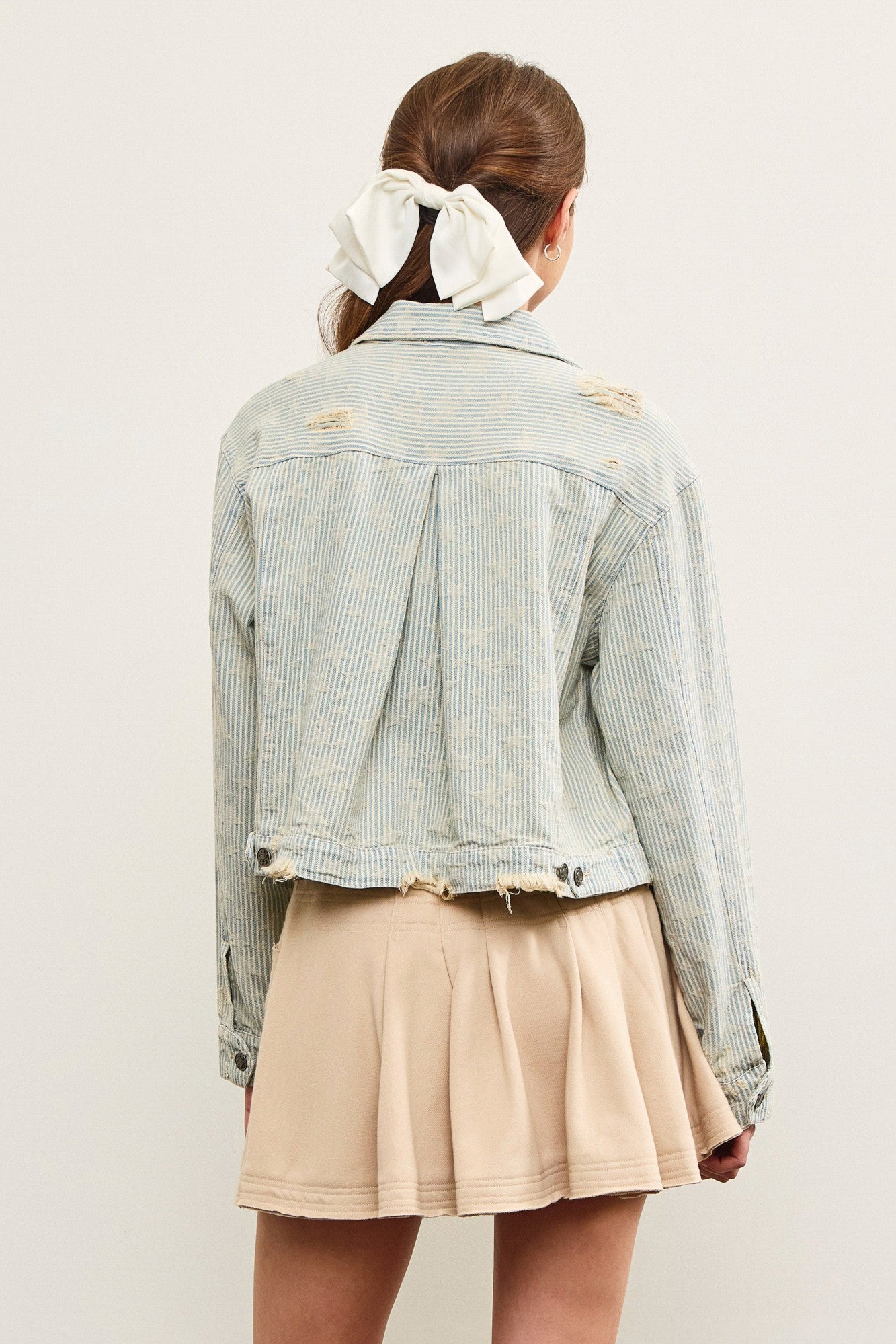 Back view of distressed hem striped denim jacket with pleated back detail
