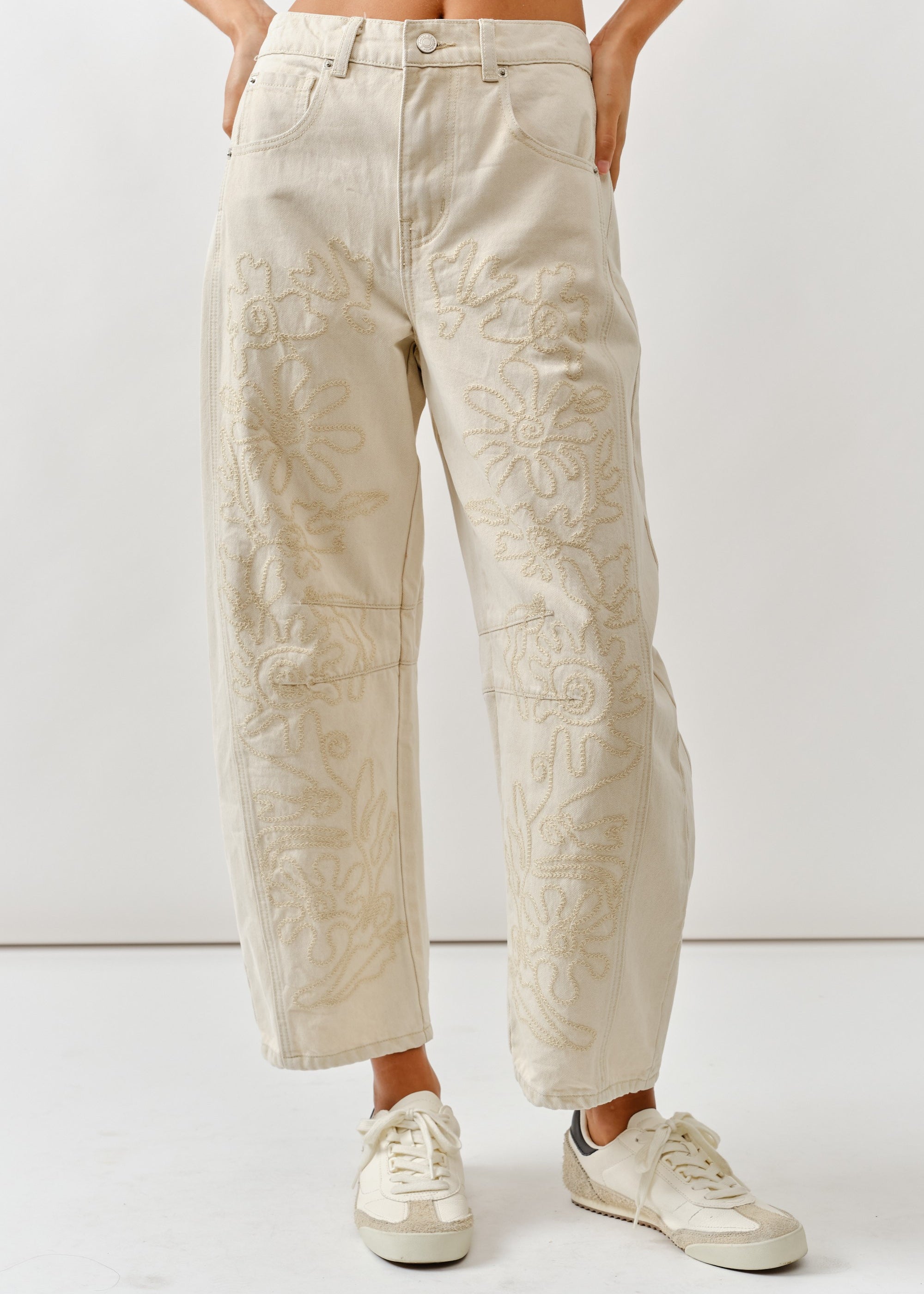 Person wearing beige embroidered pants on a white background