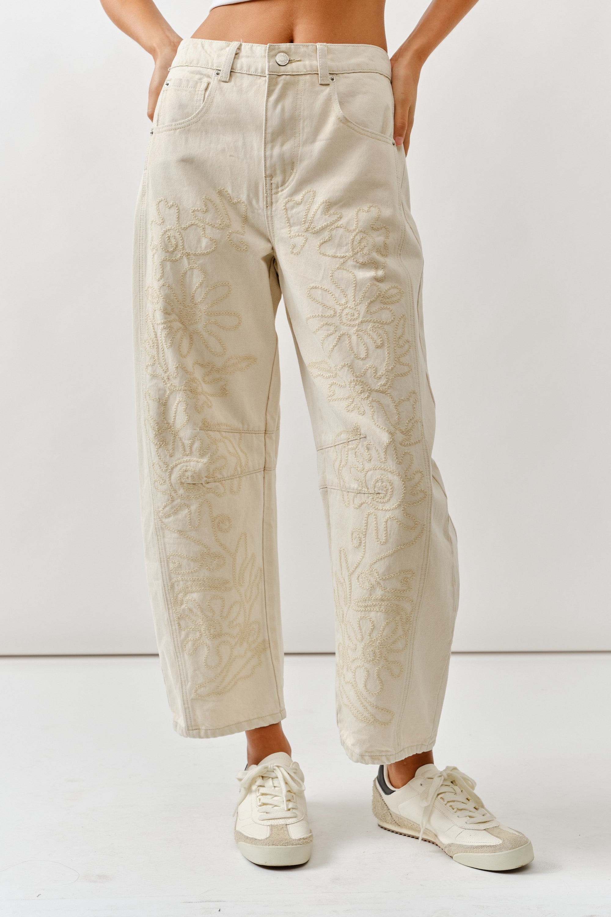 Person wearing beige embroidered pants on a white background