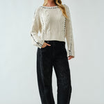 Woman wearing a white ribbed sweater and black jeans against a white background