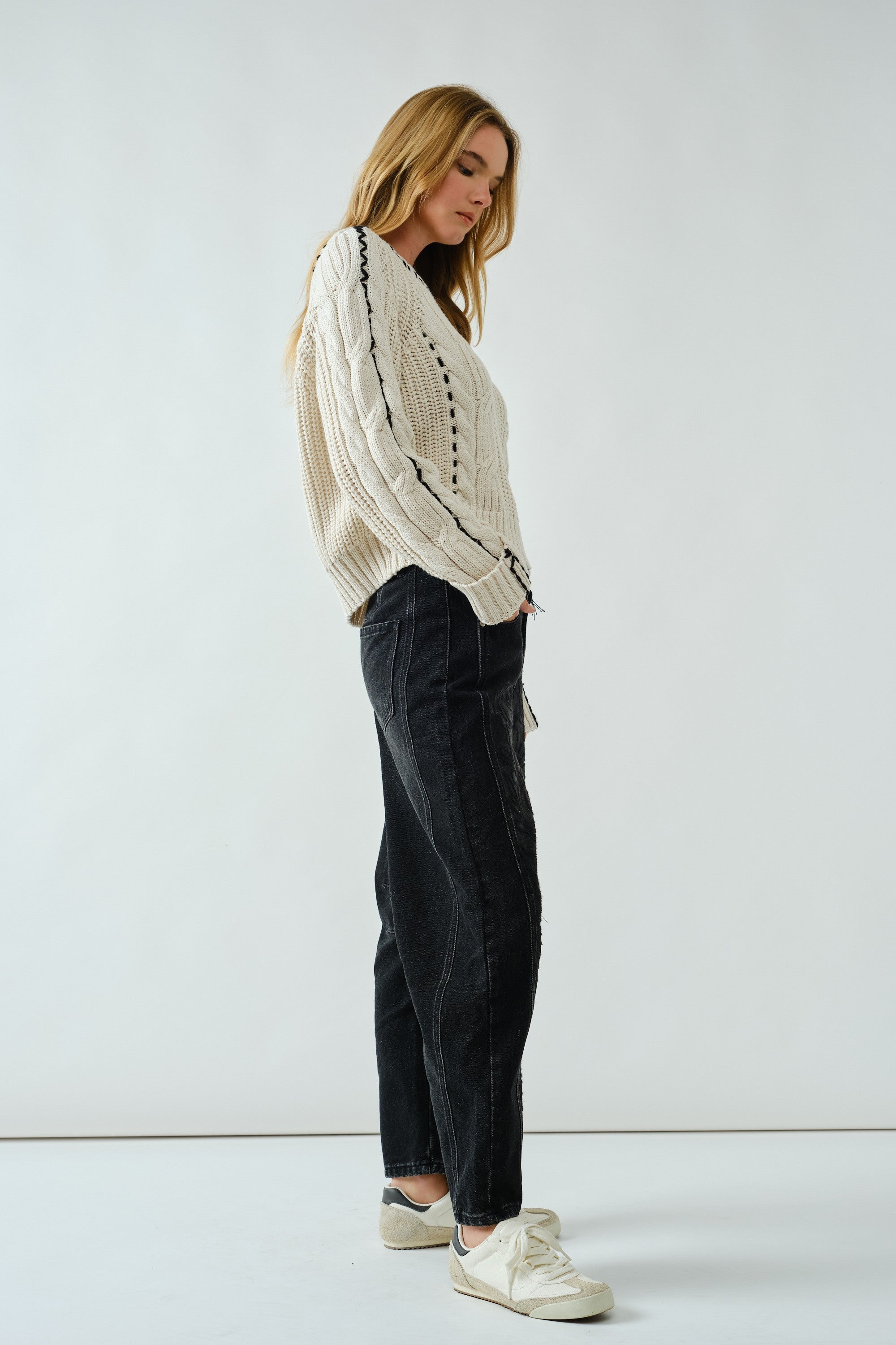 Woman wearing a white knit sweater and black pants against a white background