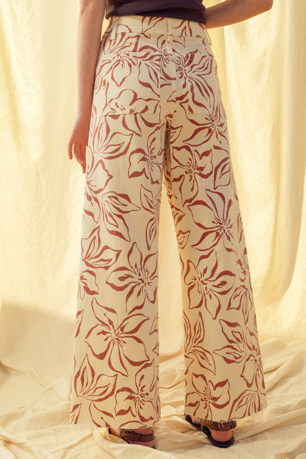 Back view of red floral print wide leg denim pants with relaxed fit and raw hem