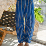 Blue pinstripe pants worn by a person in a casual setting with a chair and plant in the background.