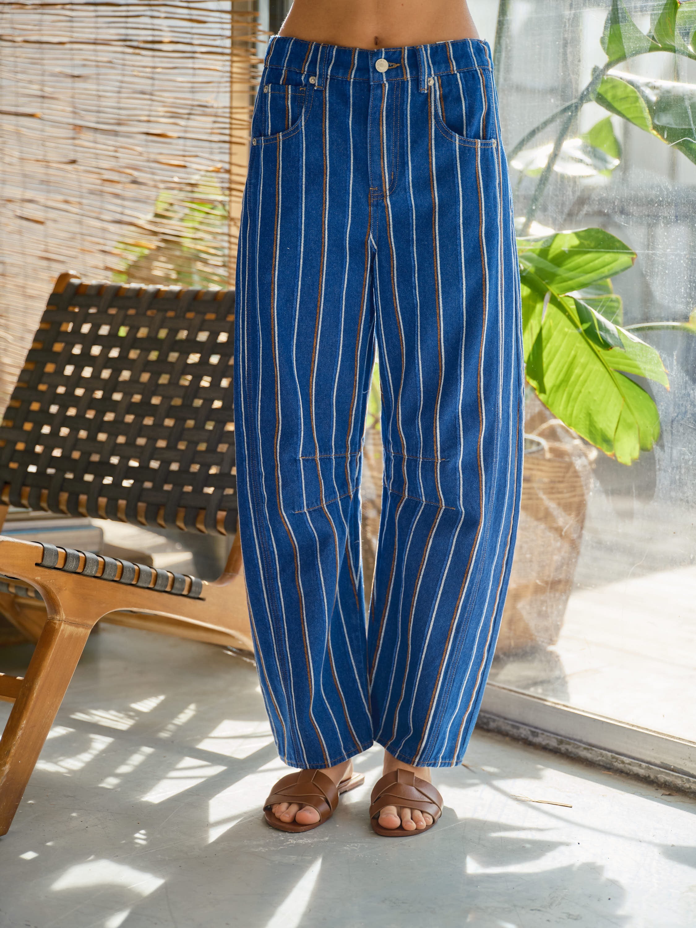 Blue pinstripe pants worn by a person in a casual setting with a chair and plant in the background.
