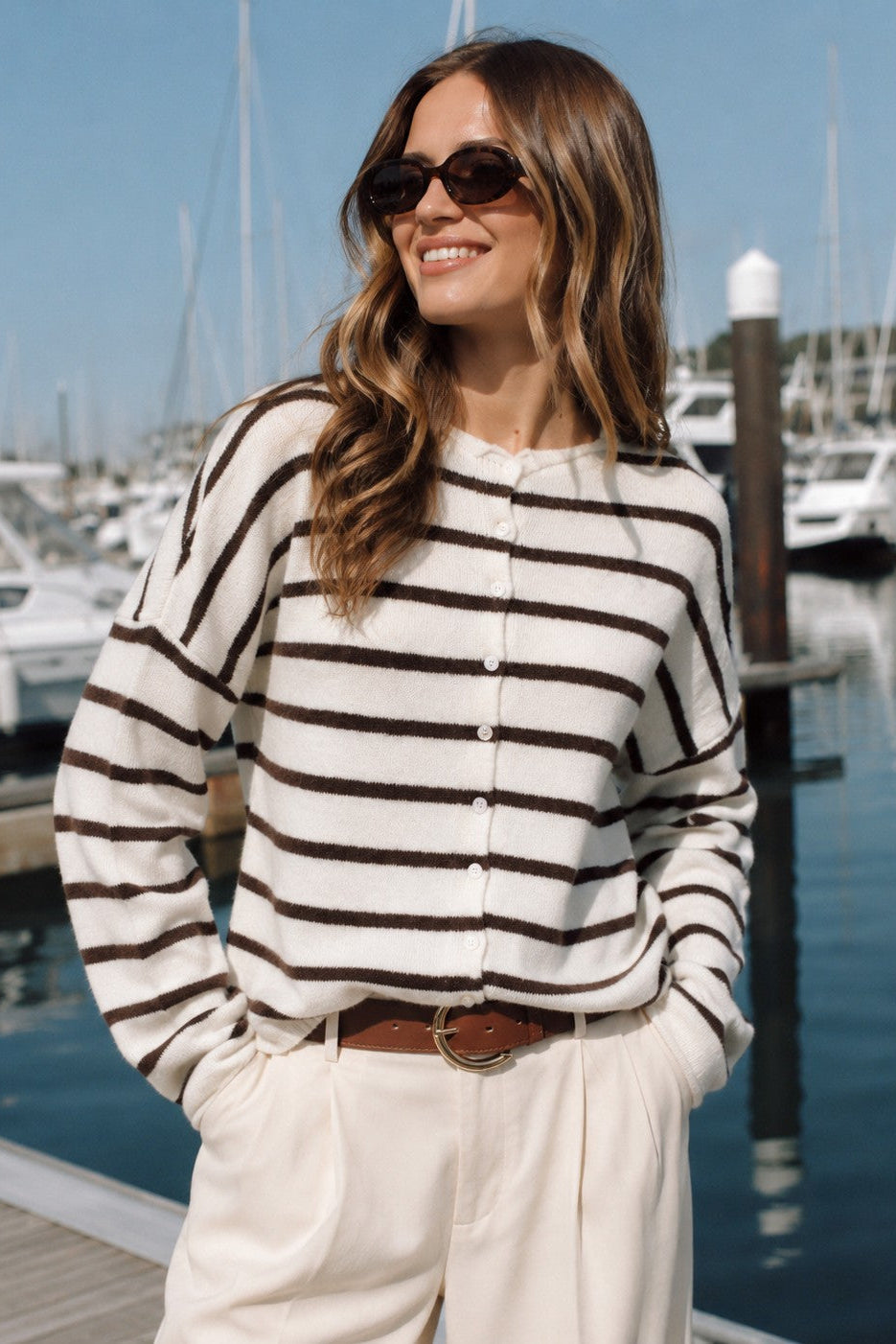 Model wearing the Hailey Button Down Cardigan in Cabana Stripe Cream-Brown at a marina