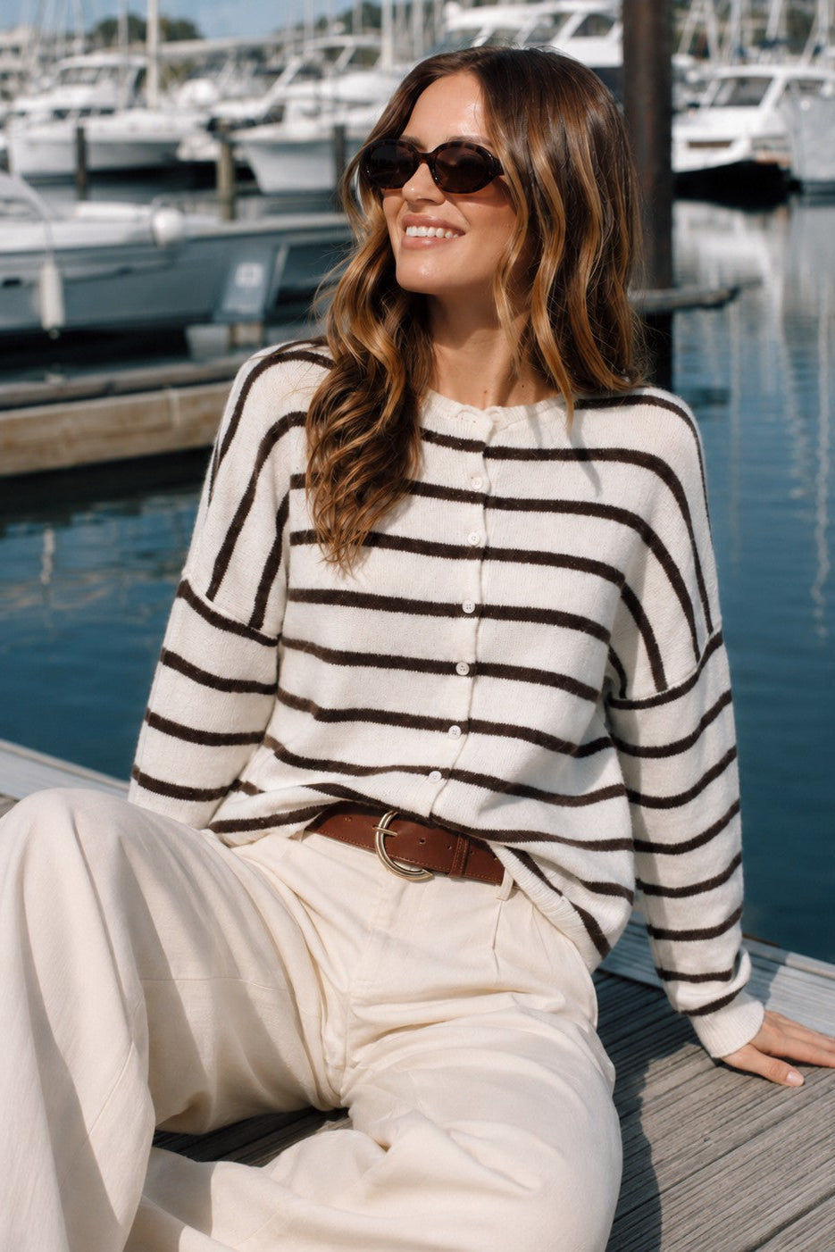Model wearing the Hailey Button Down Cardigan in Cabana Stripe Cream-Brown in a sitting lifestyle pose