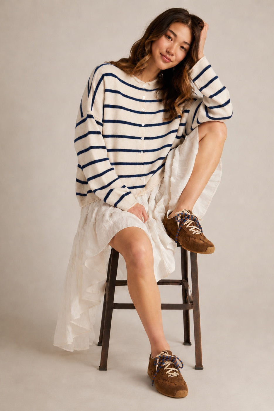 Model wearing the Hailey Button Down Cardigan in Cabana Stripe Natural-Navy in a full outfit sitting pose