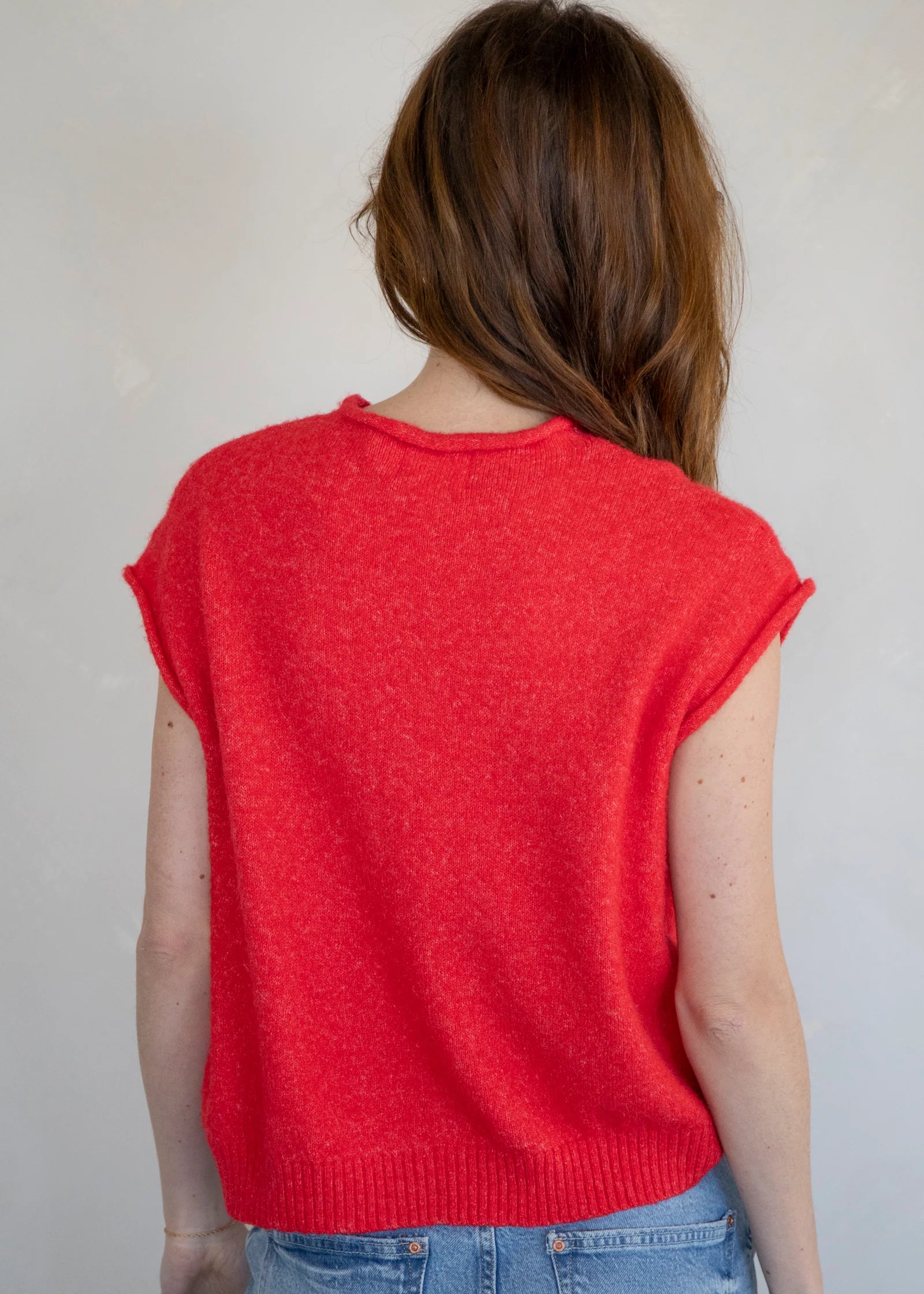 Person wearing a red sleeveless sweater against a plain background