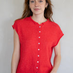 Woman wearing a red sleeveless button-up shirt against a plain background