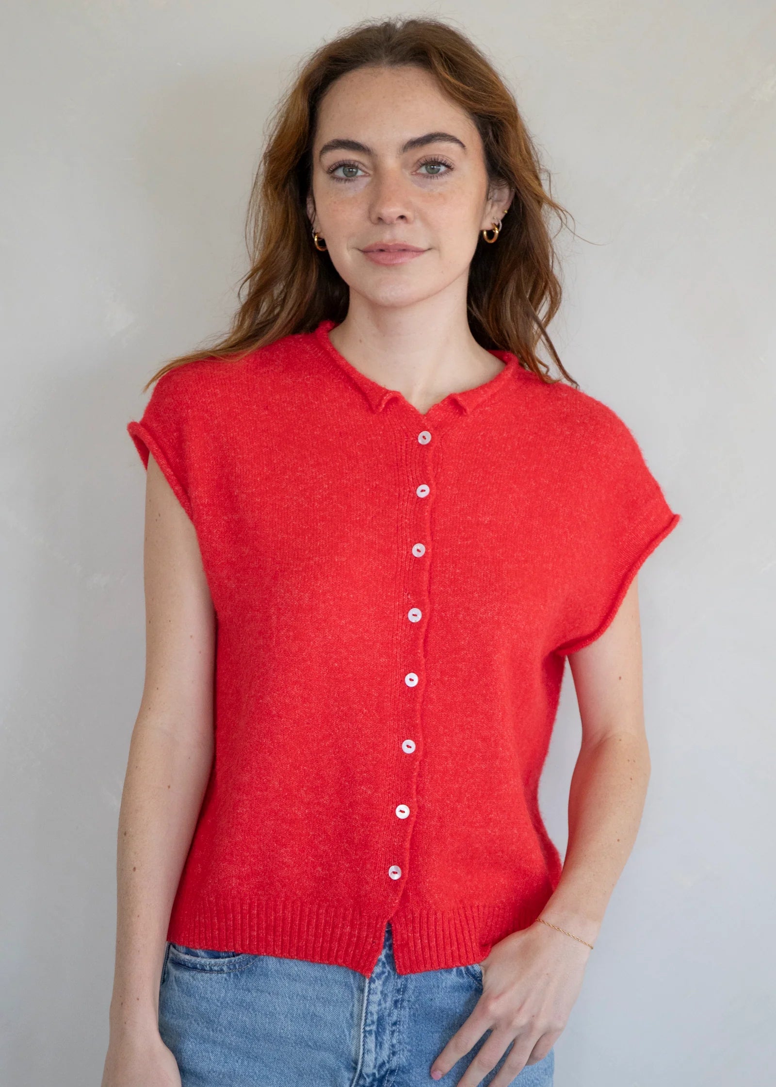 Woman wearing a red sleeveless button-up shirt against a plain background