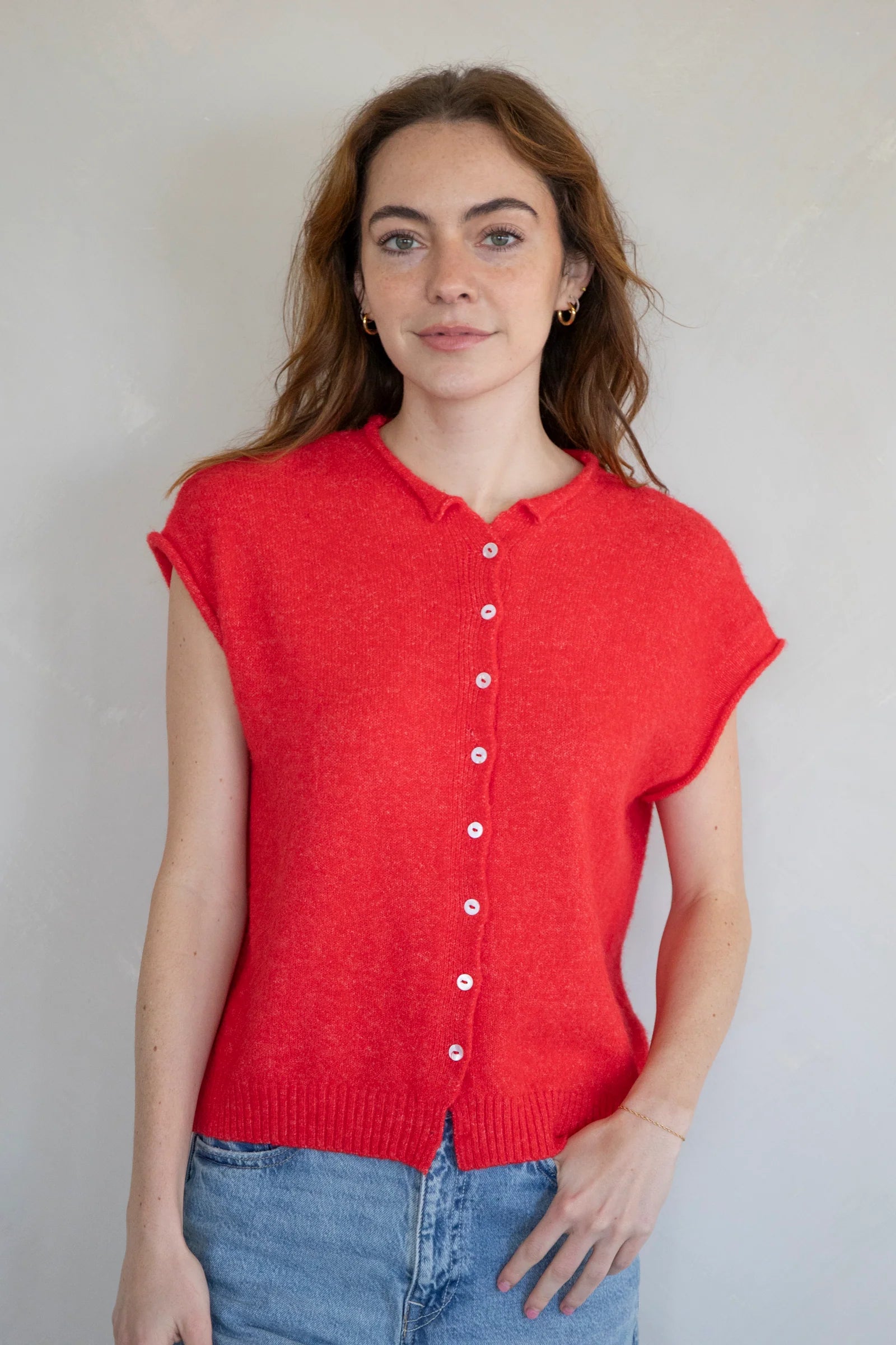 Woman wearing a red sleeveless button-up shirt against a plain background