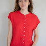 Woman wearing a red sleeveless button-up shirt against a plain background