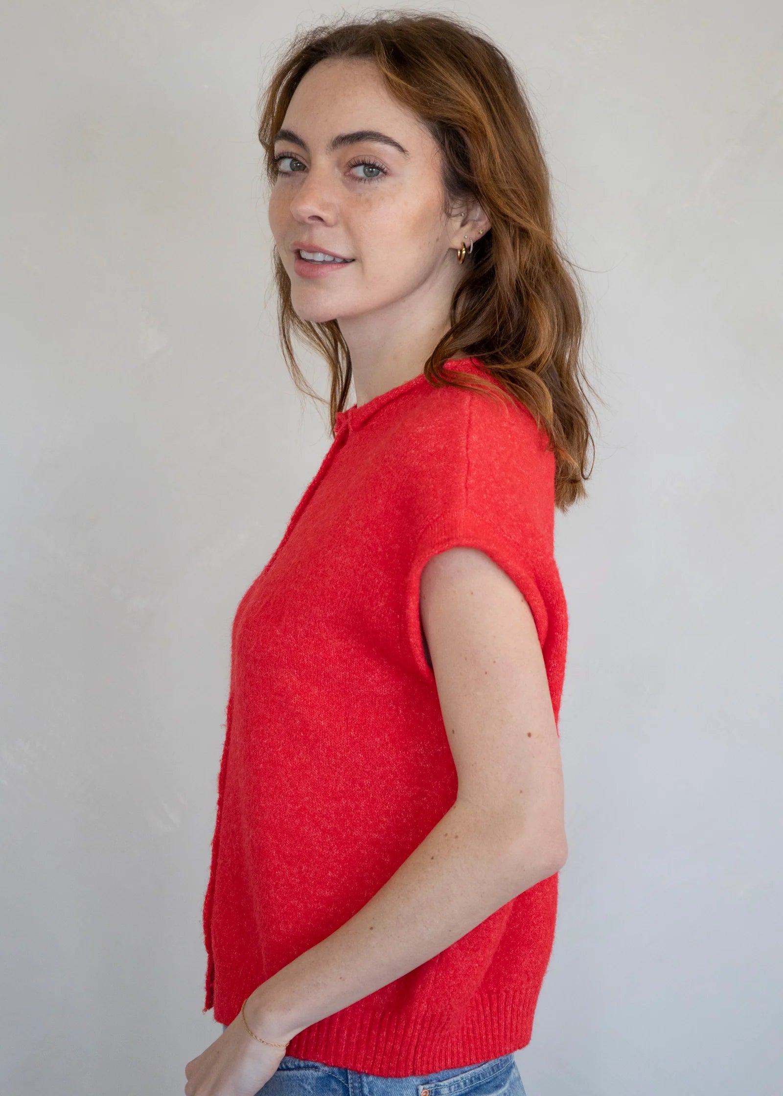 Woman wearing a red sleeveless Piper Vest Cardigan against a plain background