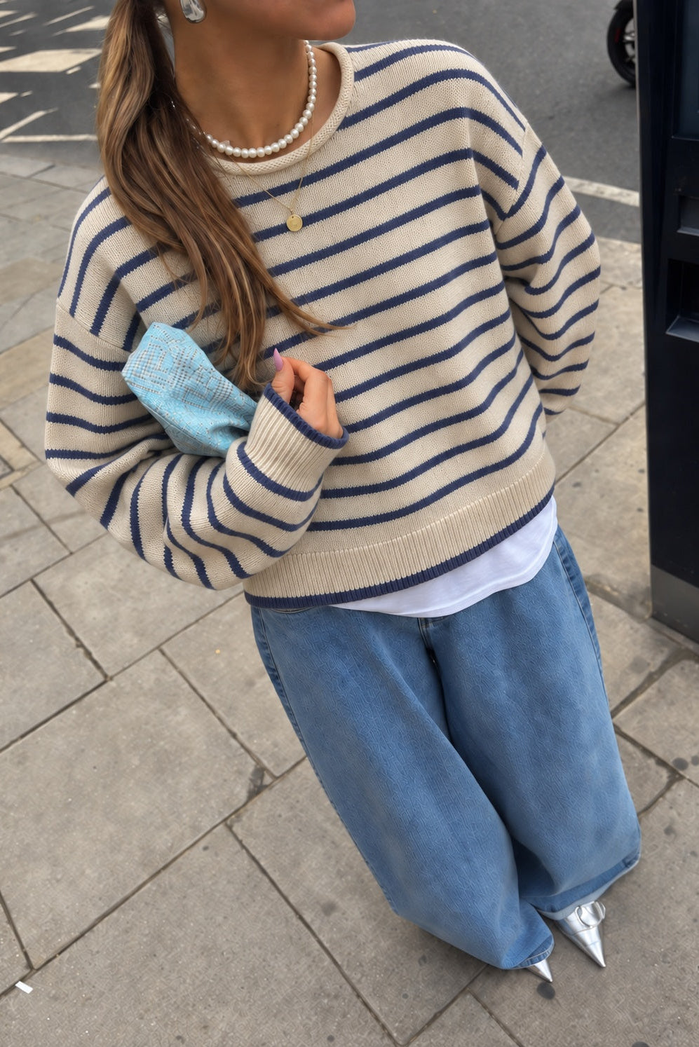 Model wearing the Harbor Striped Rollneck Sweater in light butter cream with blue stripes, dropped shoulders, and blue-tipped cuffs and hem.