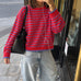 A woman takes a mirror selfie wearing a red and blue striped knit sweater, light-wash wide-leg jeans, and black shoes, carrying a black shoulder bag.