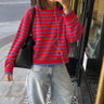 A woman takes a mirror selfie wearing a red and blue striped knit sweater, light-wash wide-leg jeans, and black shoes, carrying a black shoulder bag.