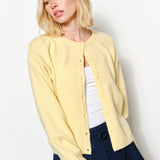woman is wearing the Harper Round-Neck Relaxed Cardigan in butter yellow showing button details and soft knit texture.