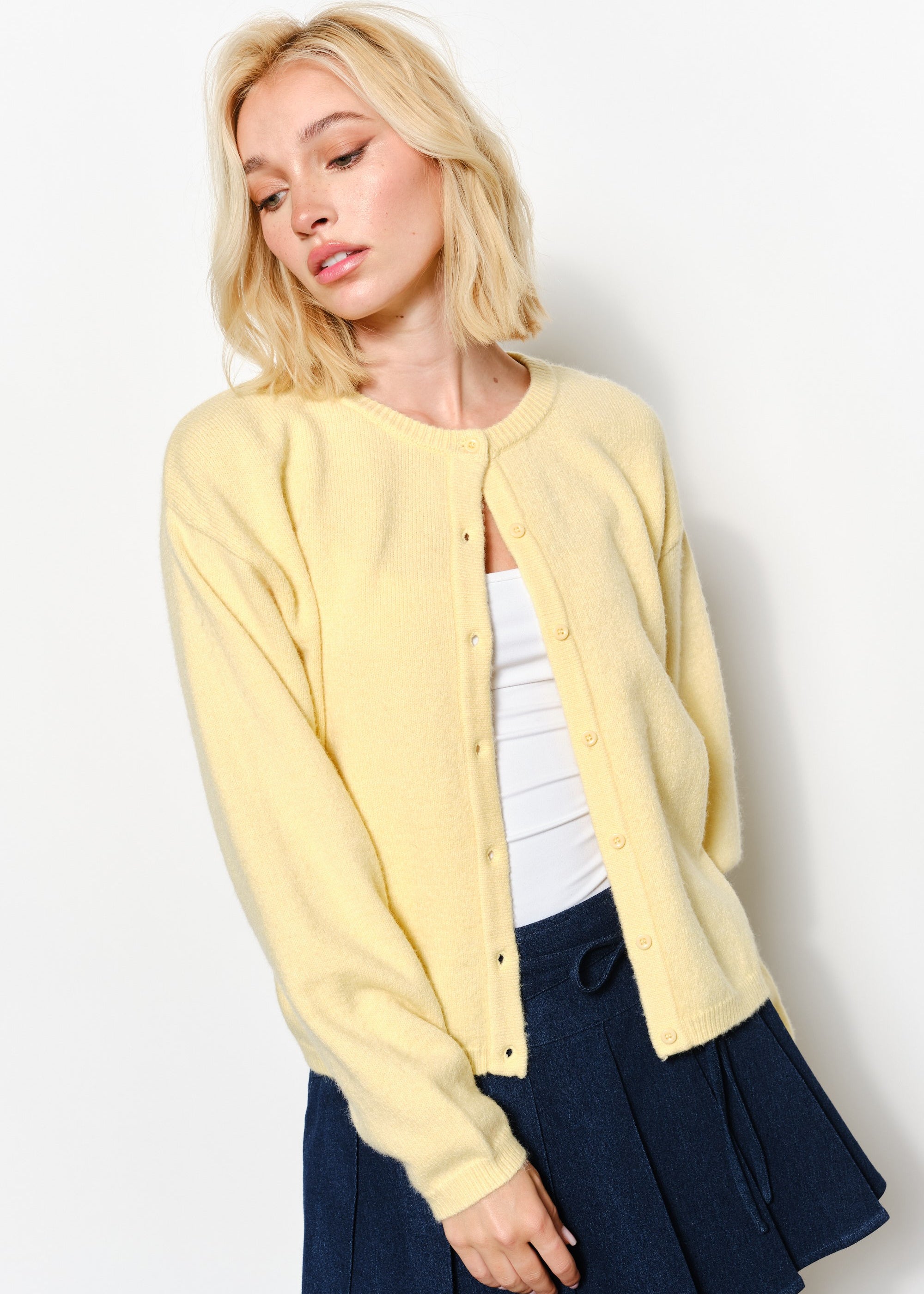 woman is wearing the Harper Round-Neck Relaxed Cardigan in butter yellow showing button details and soft knit texture.