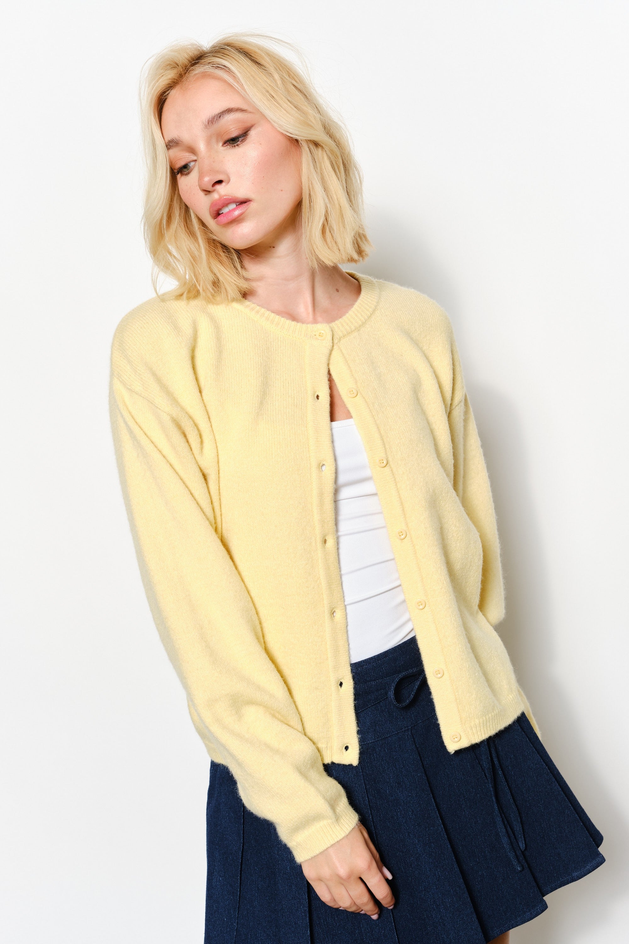 woman is wearing the Harper Round-Neck Relaxed Cardigan in butter yellow showing button details and soft knit texture.