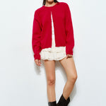 Woman wearing the Harper Round-Neck Relaxed Cardigan in red while seated — cozy and stylish women’s outfit.