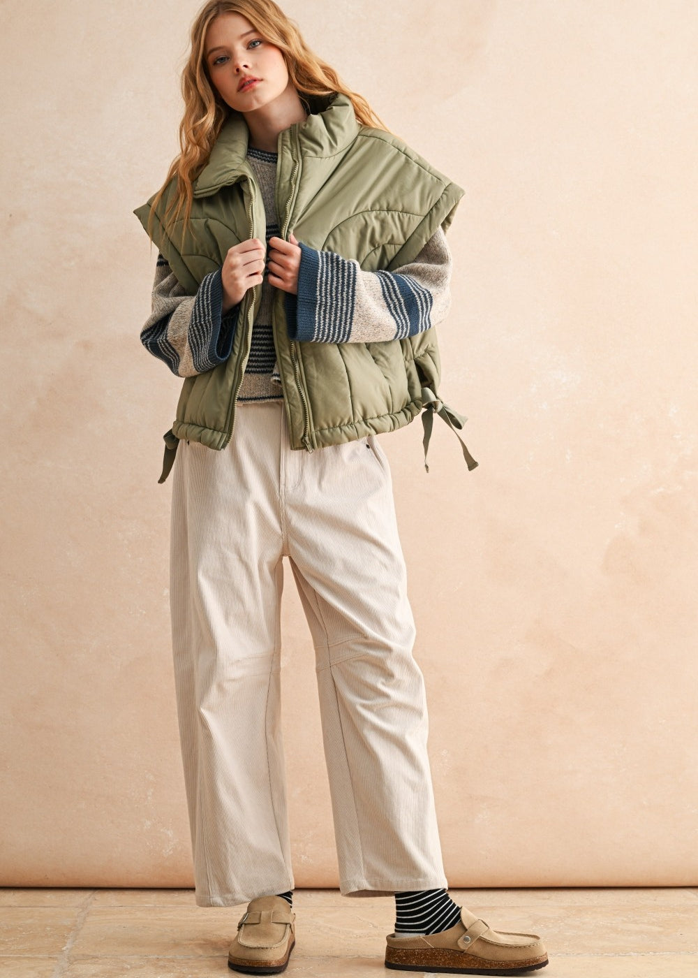 Side view of olive women’s puffer vest showing relaxed fit, adjustable hem, and high neckline — casual fall outfit.