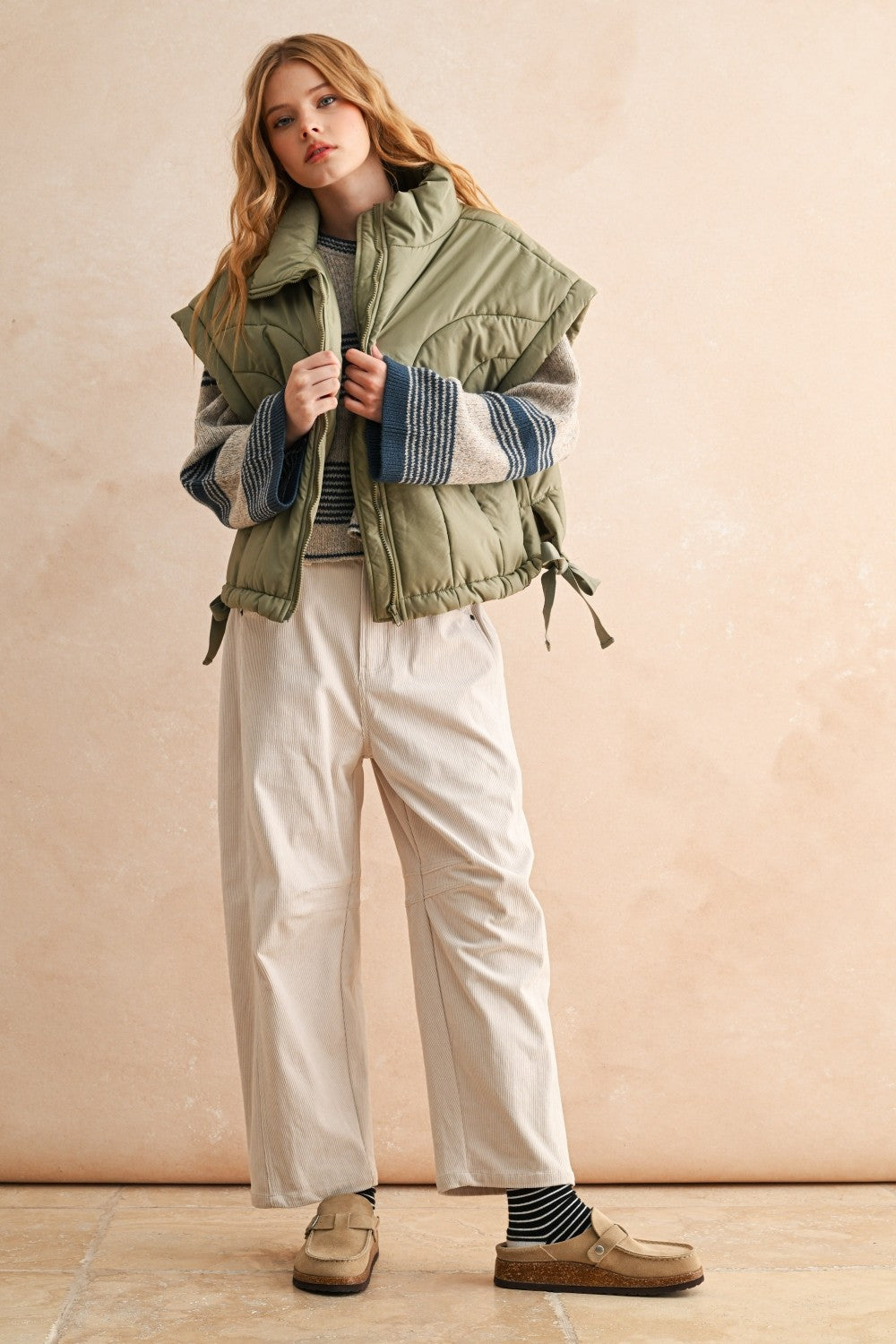 Side view of olive women’s puffer vest showing relaxed fit, adjustable hem, and high neckline — casual fall outfit.