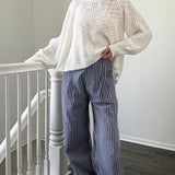 Person wearing a white sweater and blue striped pants standing in a room with a staircase.