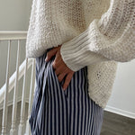 Person wearing a chunky knit sweater and striped pants indoors.