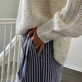Person wearing a chunky knit sweater and striped pants indoors.