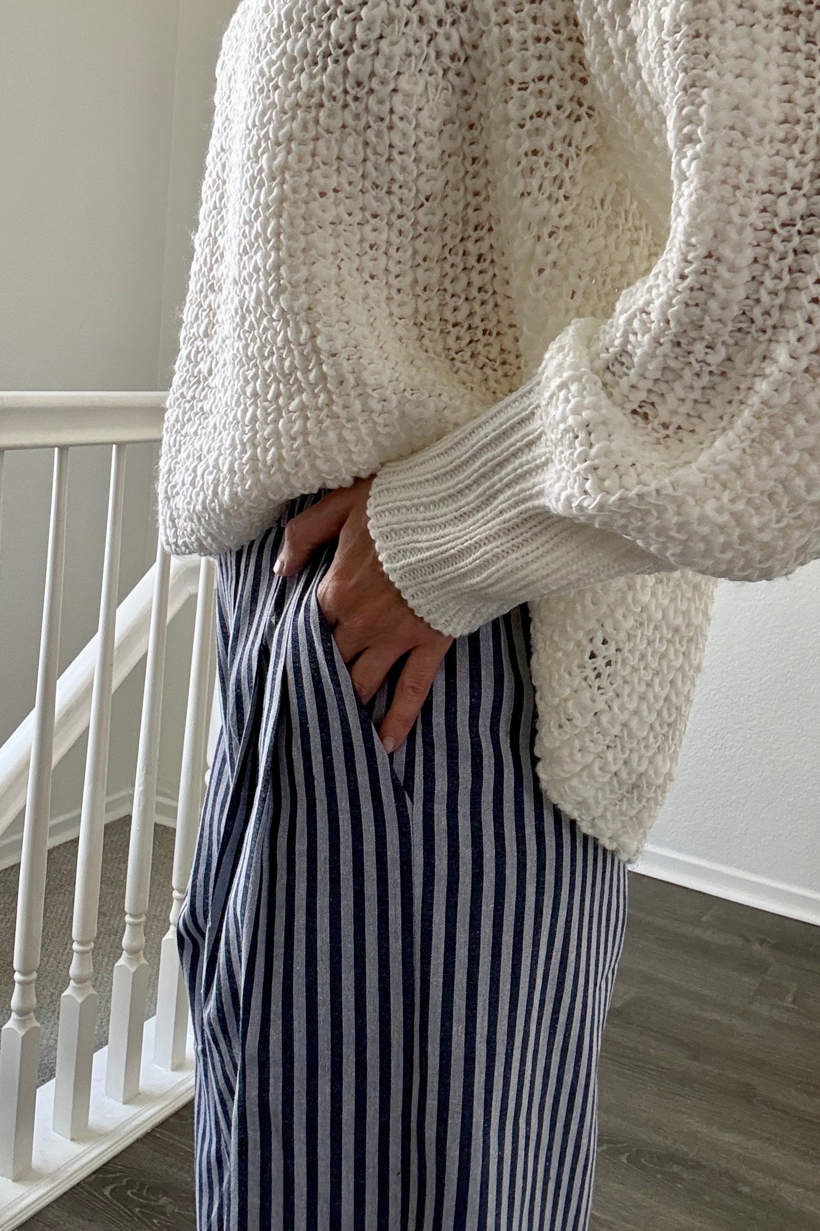 Person wearing a chunky knit sweater and striped pants indoors.