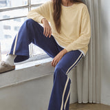 Woman seated beside a window wearing the Jetset butter yellow twofer sweatshirt with blue pants.