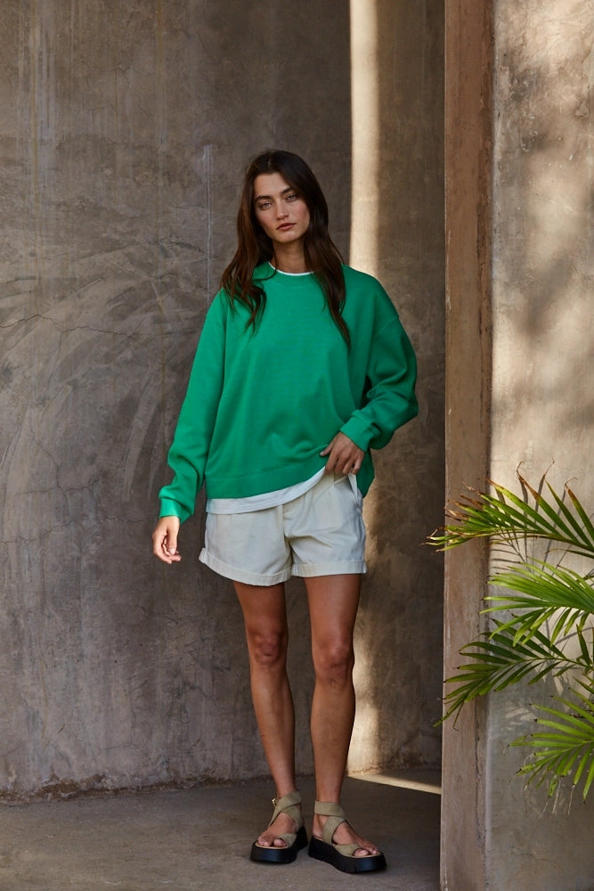 Model wearing the Jetset varsity green layered twofer sweatshirt with cream shorts.