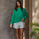 Model wearing the Jetset varsity green layered twofer sweatshirt with cream shorts.