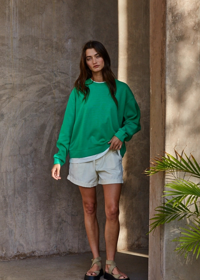 Model wearing the Jetset varsity green layered twofer sweatshirt with cream shorts.