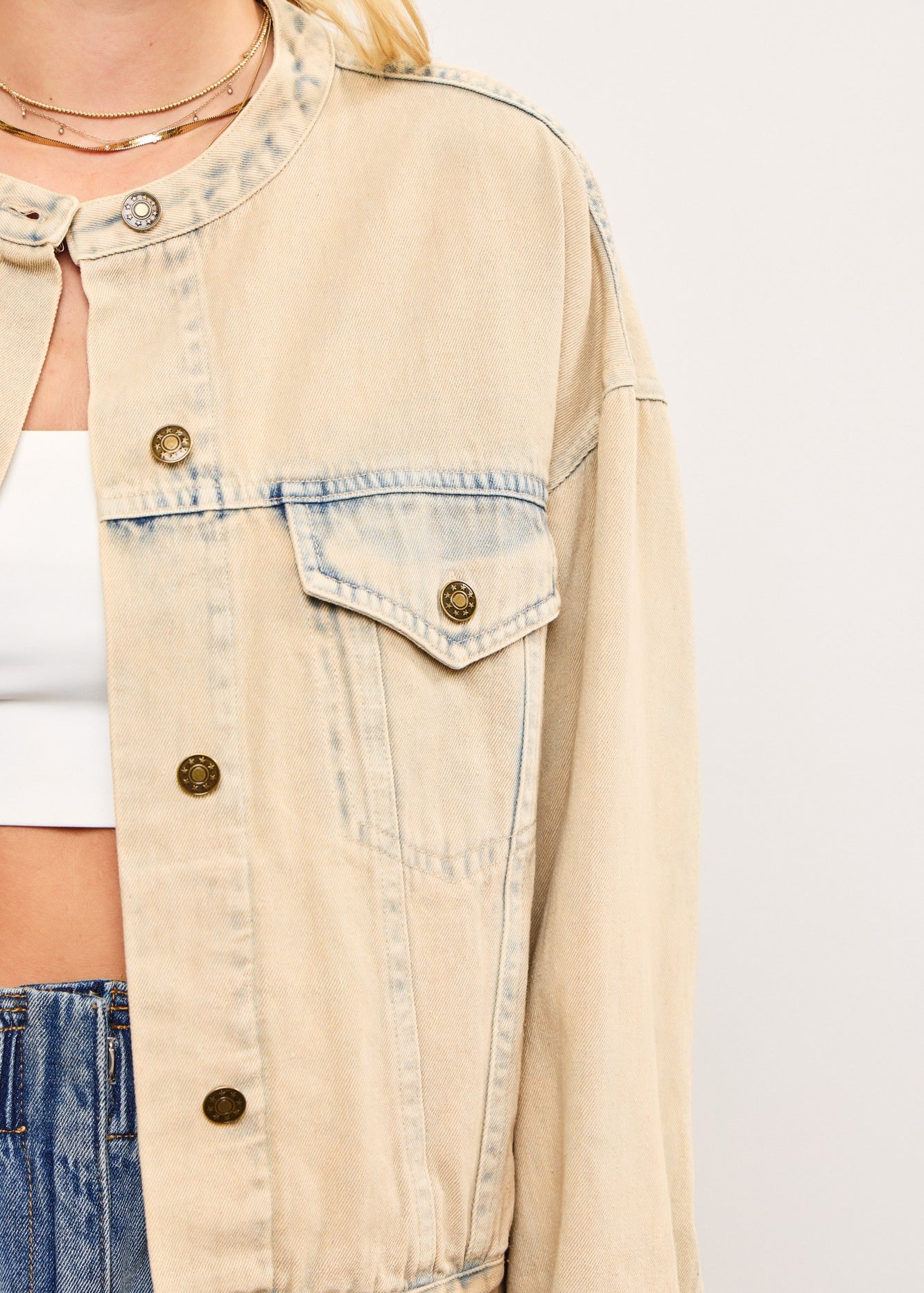 Close-up of banded collar and chest pockets on light wash denim jacket in sand denim