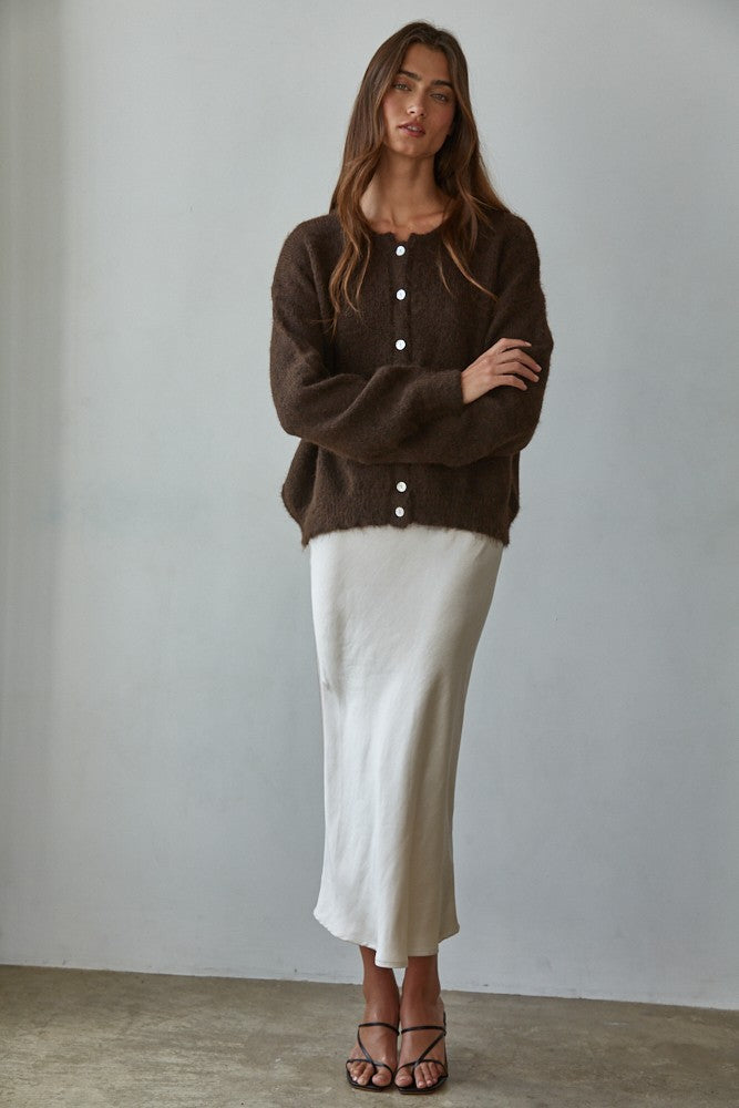 Woman wearing a brown cardigan and white skirt against a plain background