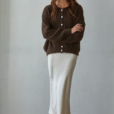Woman wearing a brown cardigan and white skirt against a plain background
