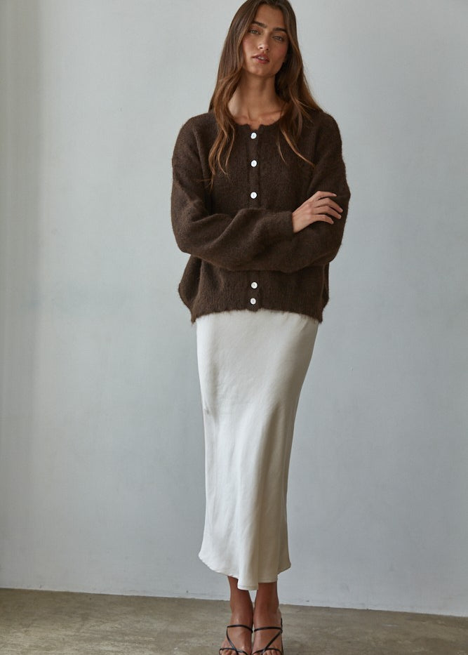 Woman wearing a brown cardigan and white skirt against a plain background