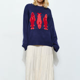 Woman wearing the Marina Fish Knit Sweater in navy — chunky oversized knit with bold red fish embroidering.