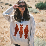 Woman wearing the Marina Fish Knit Sweater in sand — chunky oversized knit with playful red fish sardine motif