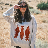Woman wearing the Marina Fish Knit Sweater in sand — chunky oversized knit with playful red fish sardine motif